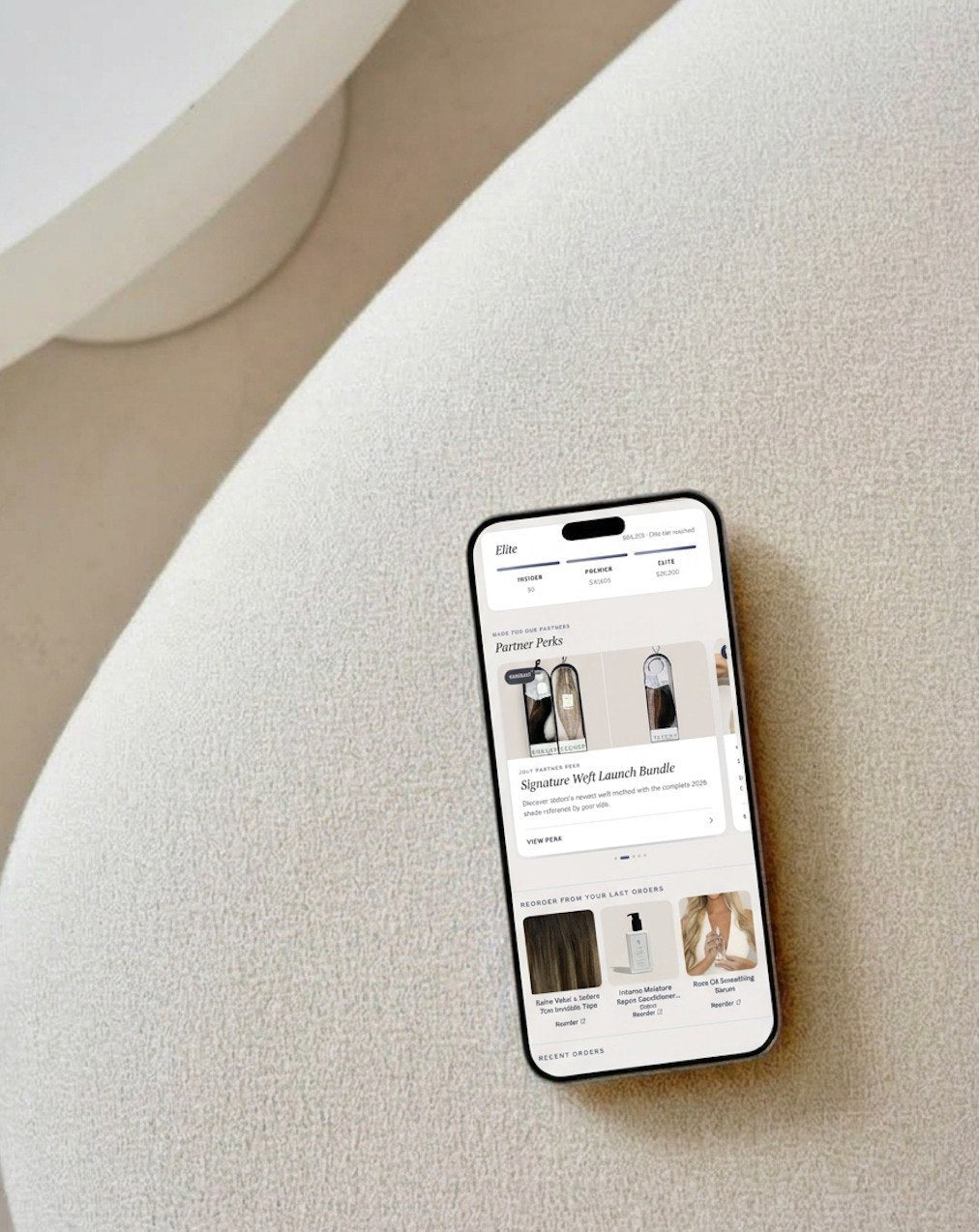 Hadrill Pro portal app open on a phone resting on an ivory boucle chair